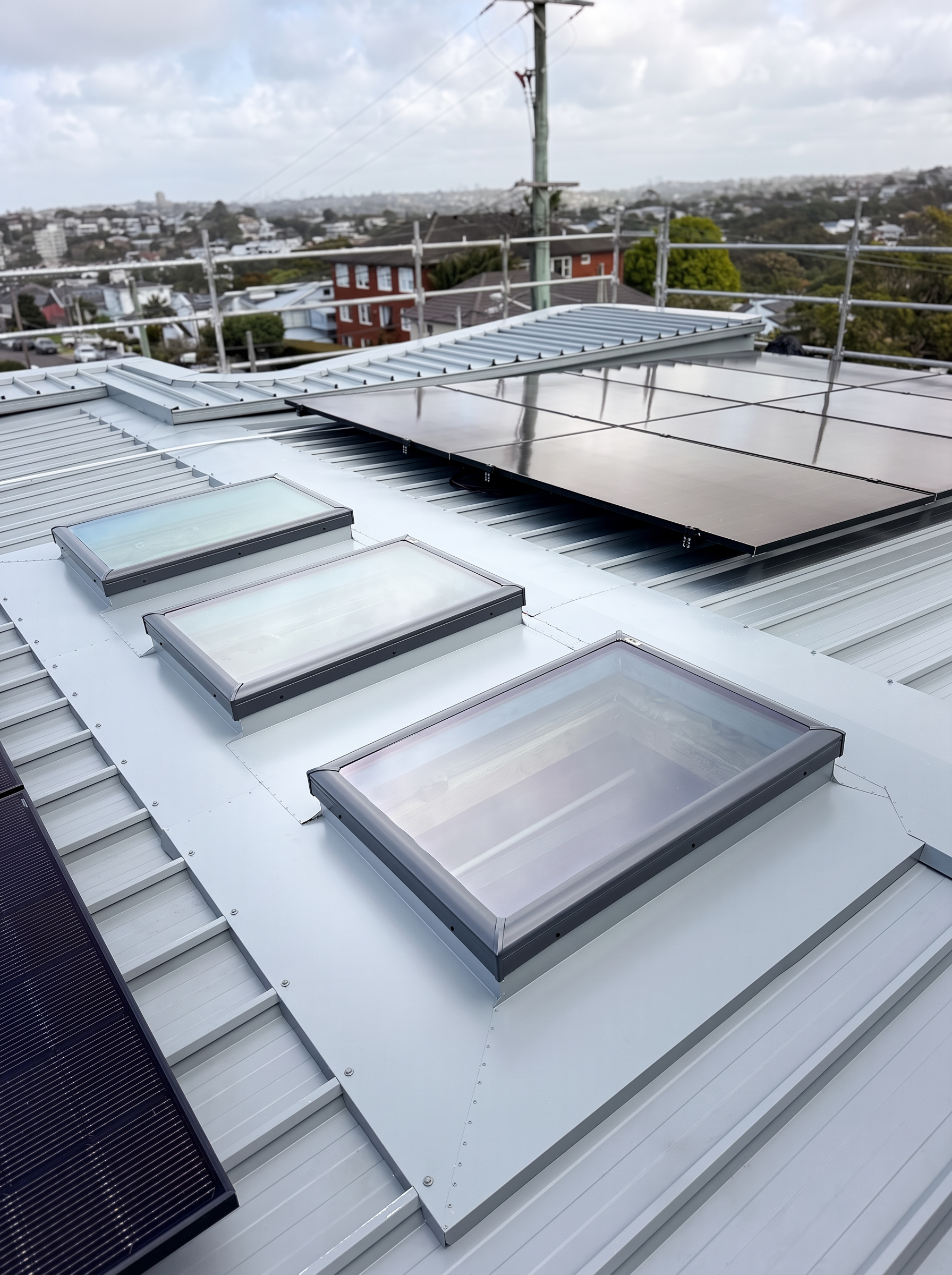 Three skylights integrated into a silver metal roof beside solar panels